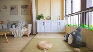 Una sala de estar acogedora con un sofá, un esterilla de tatami, una mesita y una cocina con armarios y una ventana.