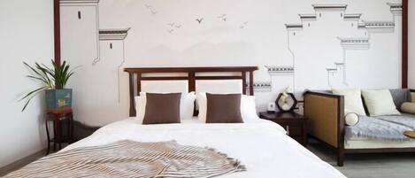 A bedroom with a large bed, a nightstand, a sofa, a wall mural, and a potted plant.