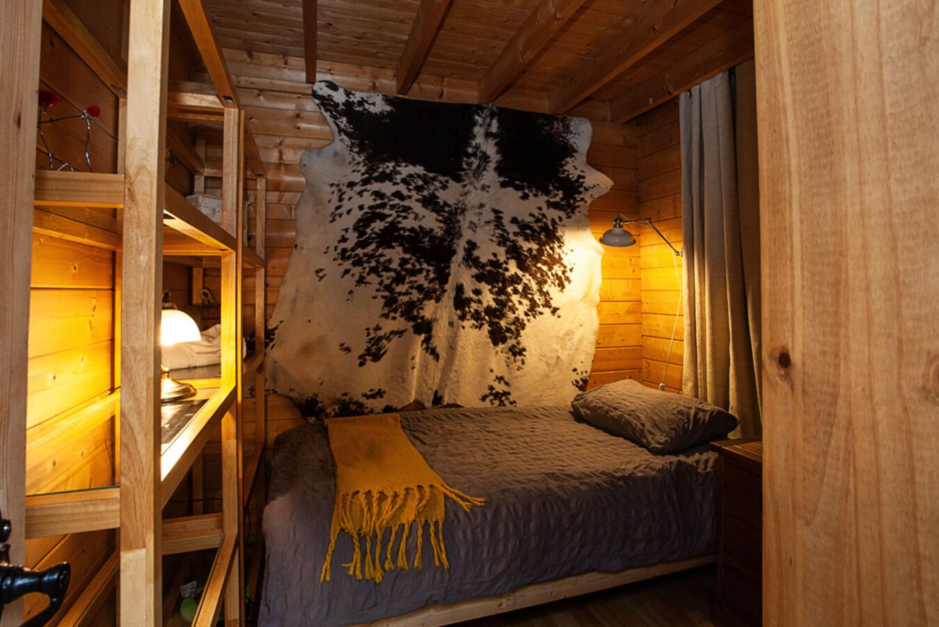 Ein gemütliches Blockhäuschenzimmer mit einem Bett, einer Holzablage und einem großen Kuhfellstück an der Wand.