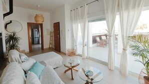 Un salon spacieux avec un canapé, une table basse en verre et une vue sur le balcon extérieur.