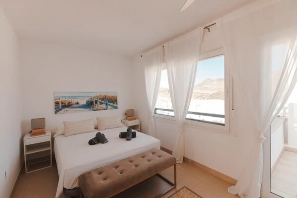 A bedroom with a bed, a bench, a nightstand, a painting, and a window with curtains. - Spanish villa in Cabo de Gata . 10 min from the beach. Private saltwater pool. . (NIJAR)