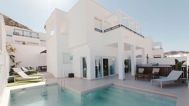 Un bâtiment moderne de couleur blanche, doté d’une piscine, de chaises longues et d’un espace bar.