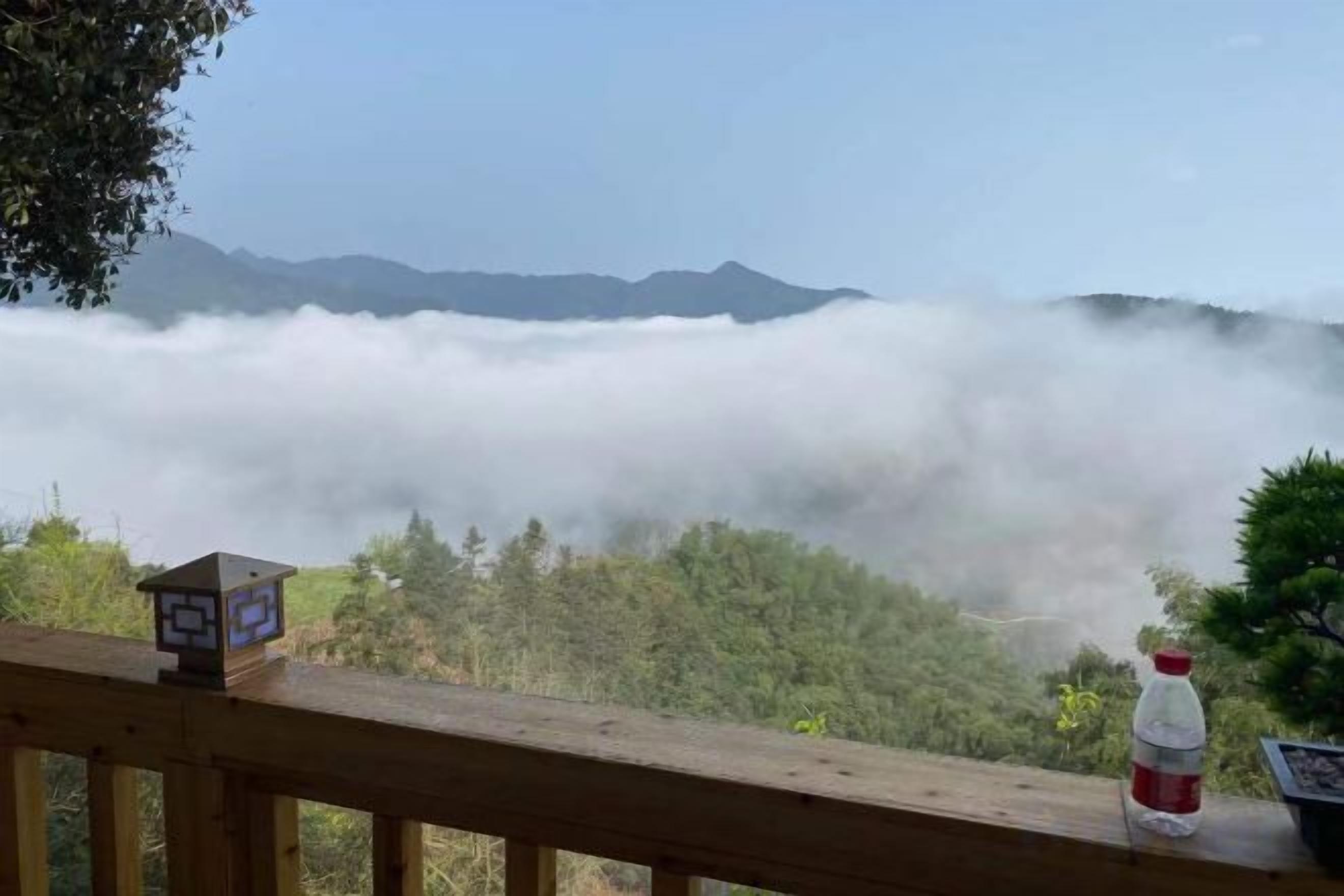 A wooden deck with a view of a forest and mountains, a bottle, and a small house-like object.