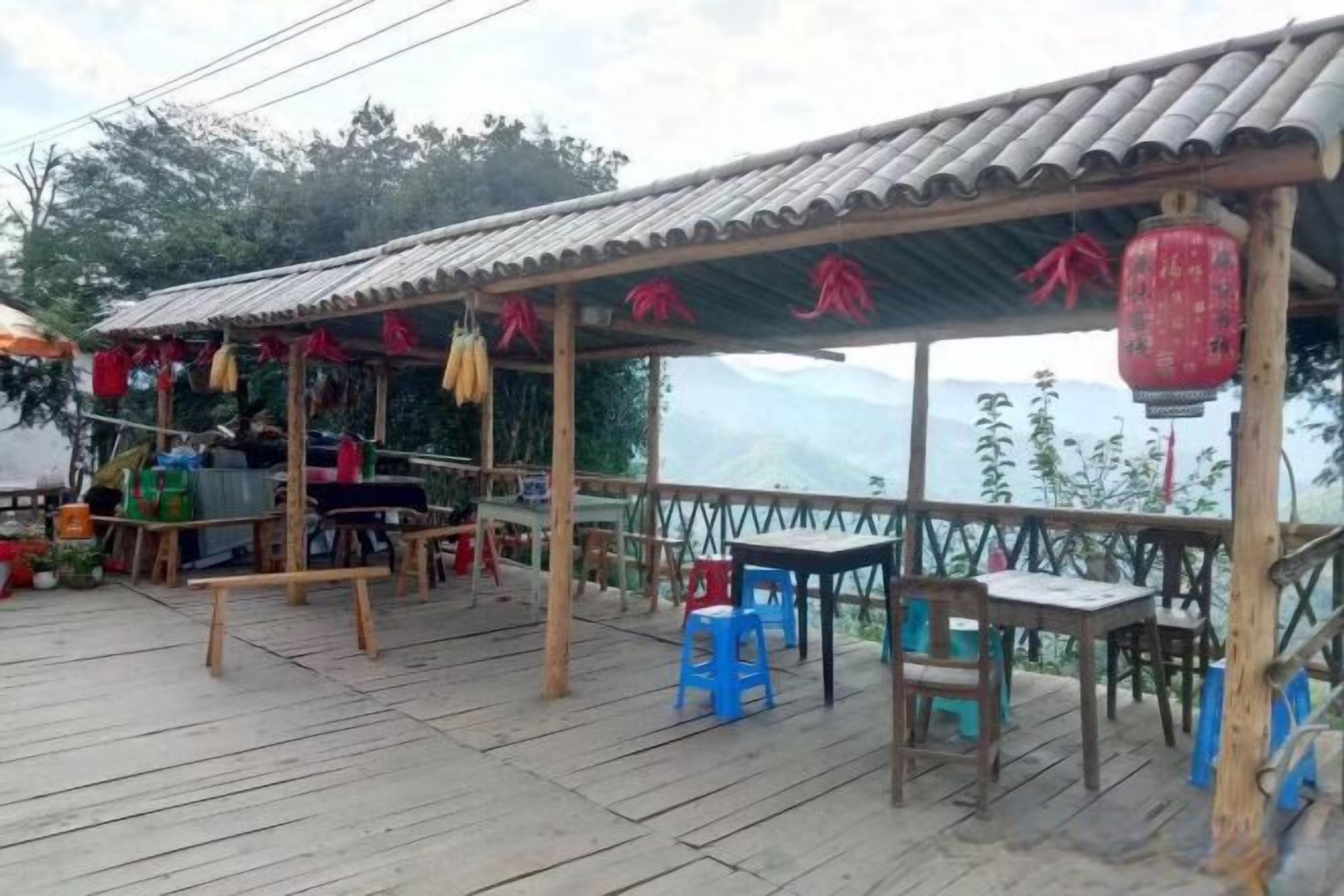 A covered outdoor seating area with tables and chairs, a wooden deck, and a view of the mountains.