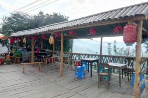 A covered outdoor seating area with tables and chairs, a wooden deck, and a view of the mountains. - Mulihong Yuanwei Inn (Xiuning)