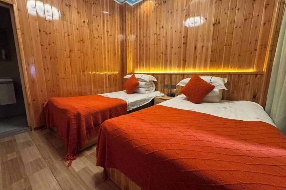 A room with wooden panel walls, two beds with red bedding, and a wooden floor.