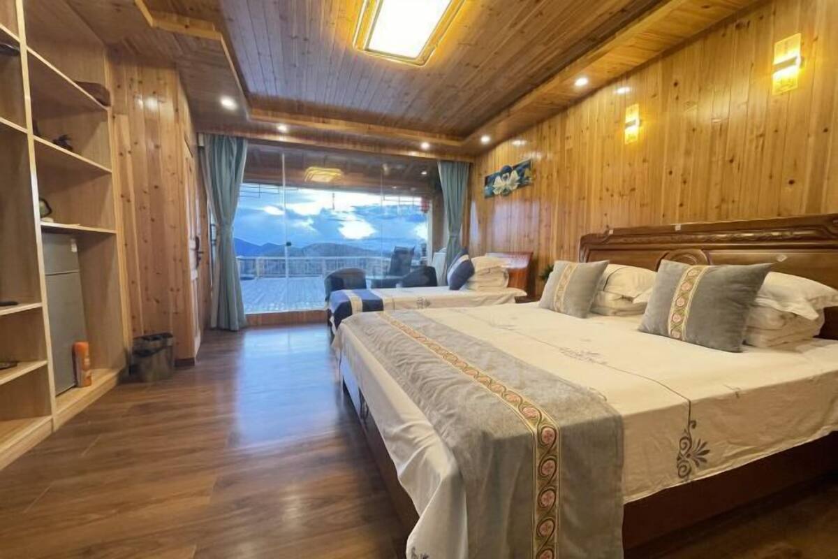 A wooden-paneled room with a large bed, a view through a window, and a shelf with items.
