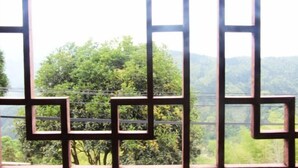 A window with a geometric metal frame, offering a view of lush greenery and distant hills. - Mulihong Yuanwei Inn (Xiuning)