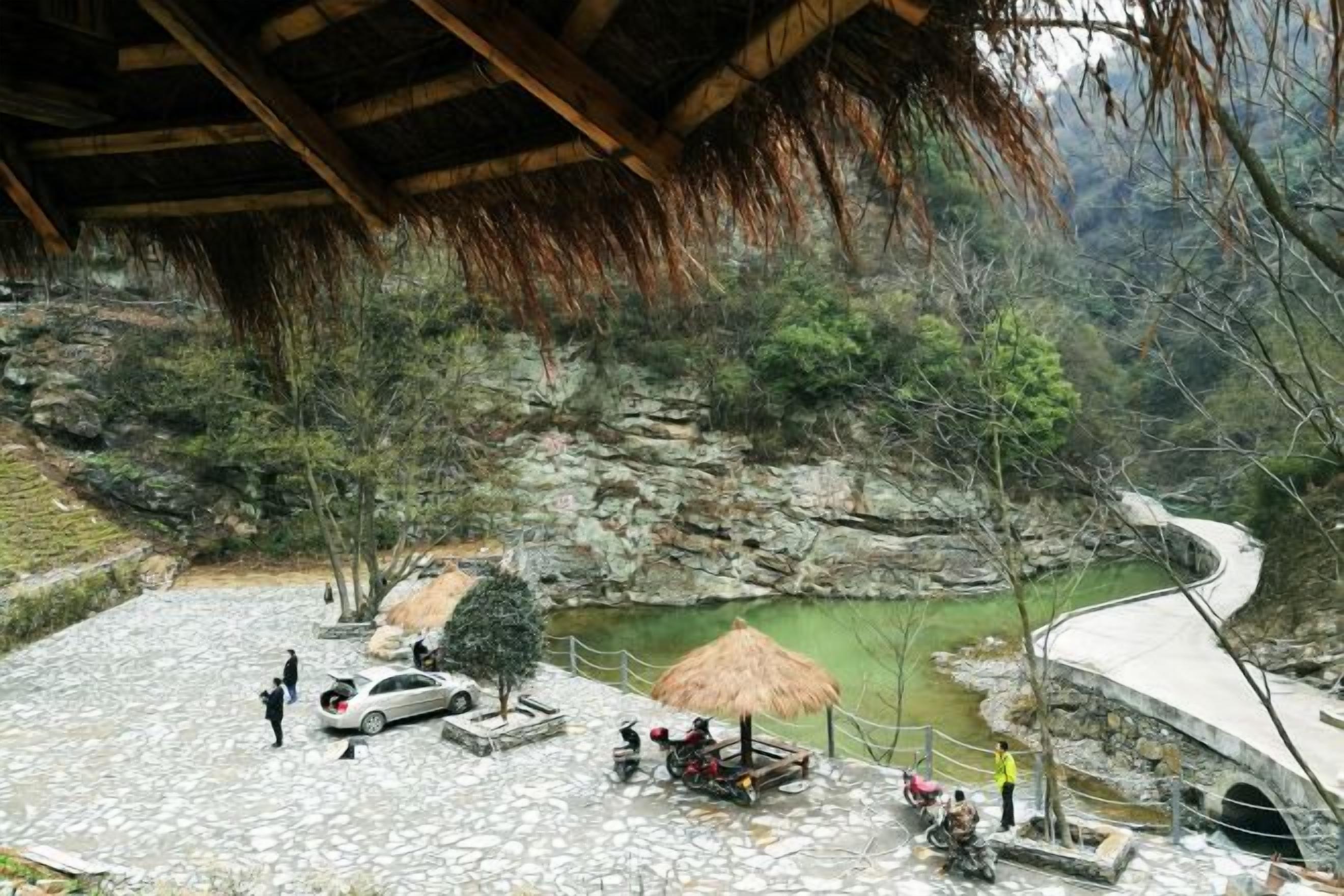 Un patio de piedra con un pabellón de techo de paja, un estanque pequeño y un sendero curvo.