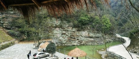 Un patio de piedra con un pabellón de techo de paja, un estanque pequeño y un sendero curvo.