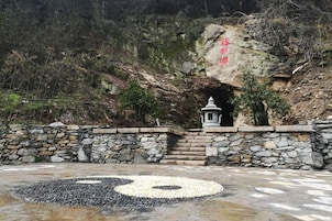 A traditional stone structure with a circular design on the ground, a small shrine, and a rocky hillside in the background.