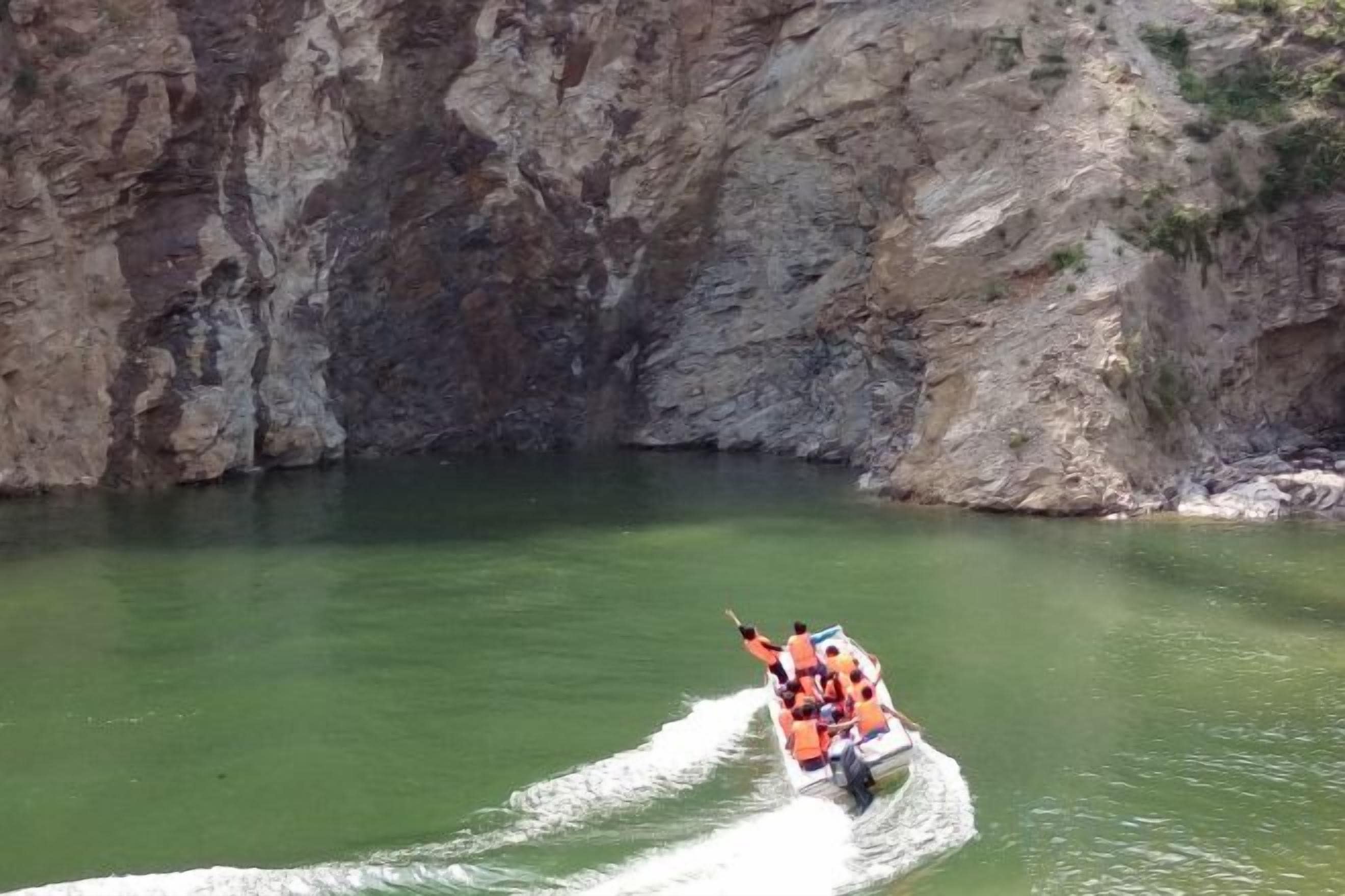 Een groep mensen in een oranje boot op een rivier, omringd door rotsachtige kliffen.