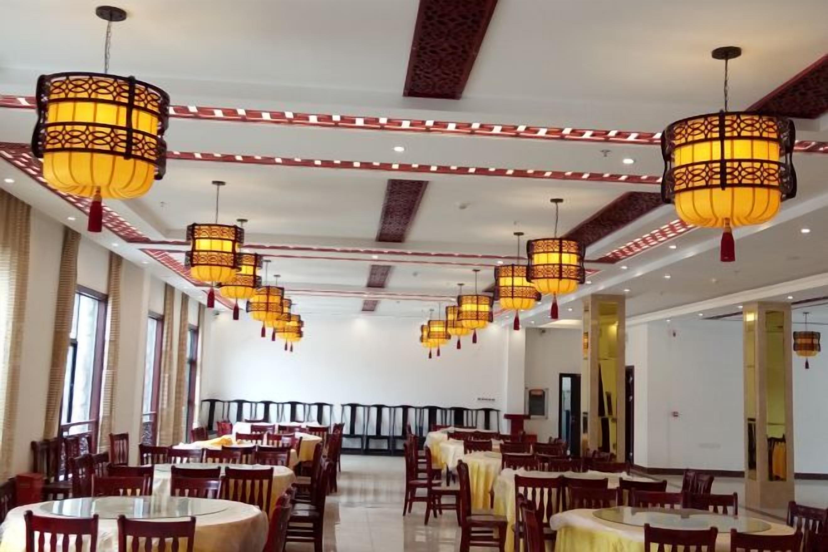 A spacious dining area with multiple tables and chairs, ornate hanging lamps, and a high ceiling with decorative elements.