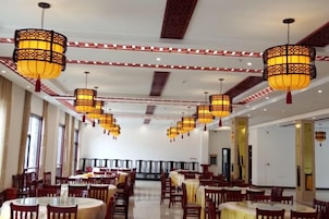 A spacious dining area with multiple tables and chairs, ornate hanging lamps, and a high ceiling with decorative elements.