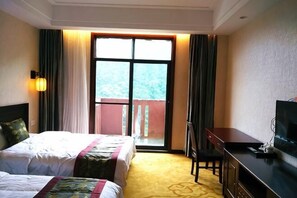A hotel room with two beds, a desk, a TV, and a balcony with a view.