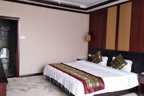 Quarto de hotel com uma cama grande, cabeceira de madeira, mesa de cabeceira e uma pequena luminária.