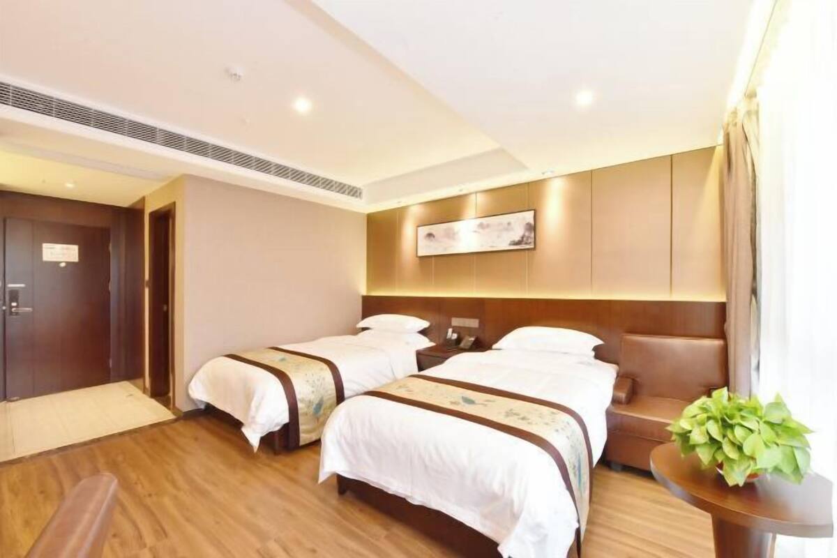 A hotel room with two beds, a wooden floor, a headboard with a painting, and a small table with a plant.