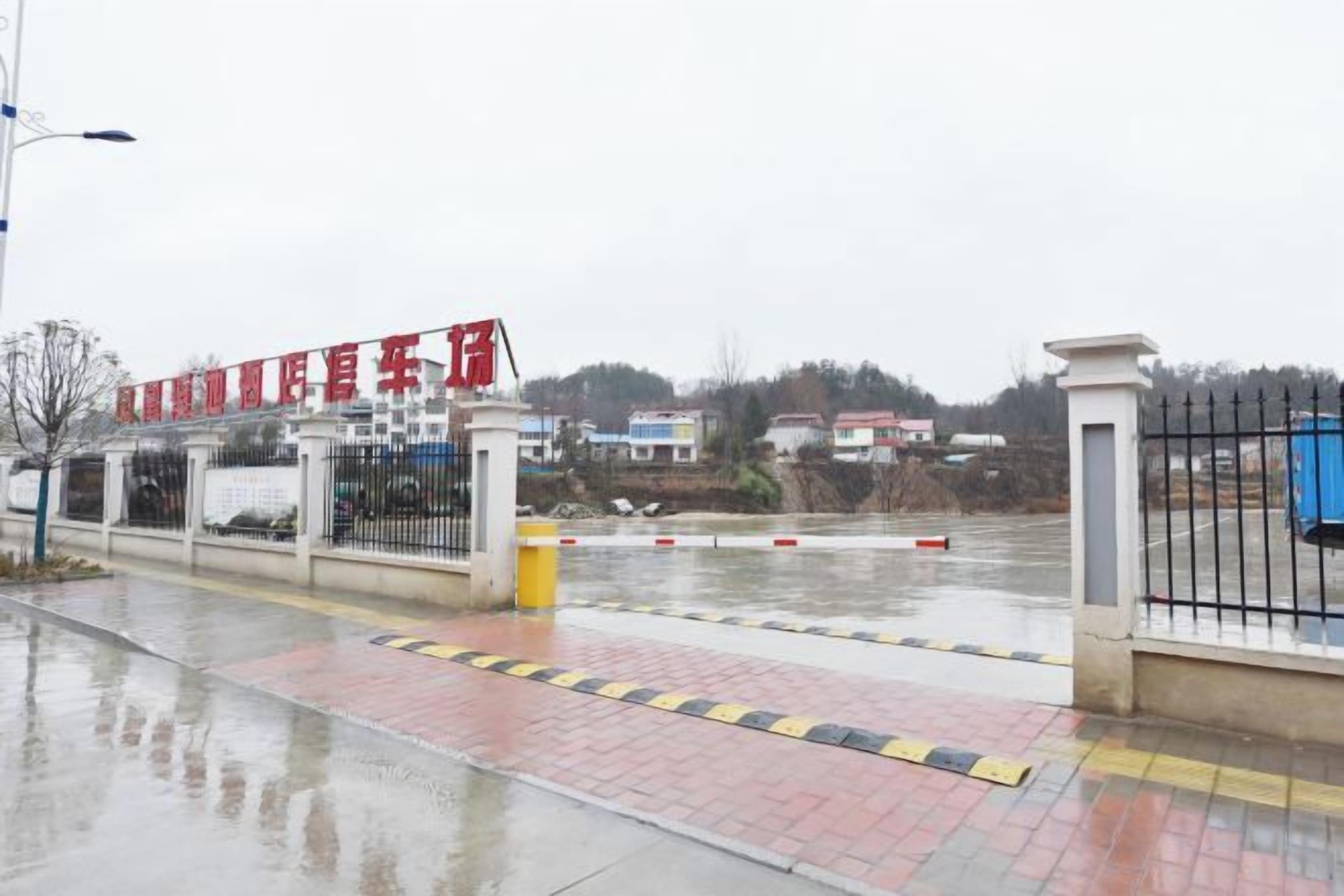 A gated entrance with a red sign, a metal fence, and a wet pavement.