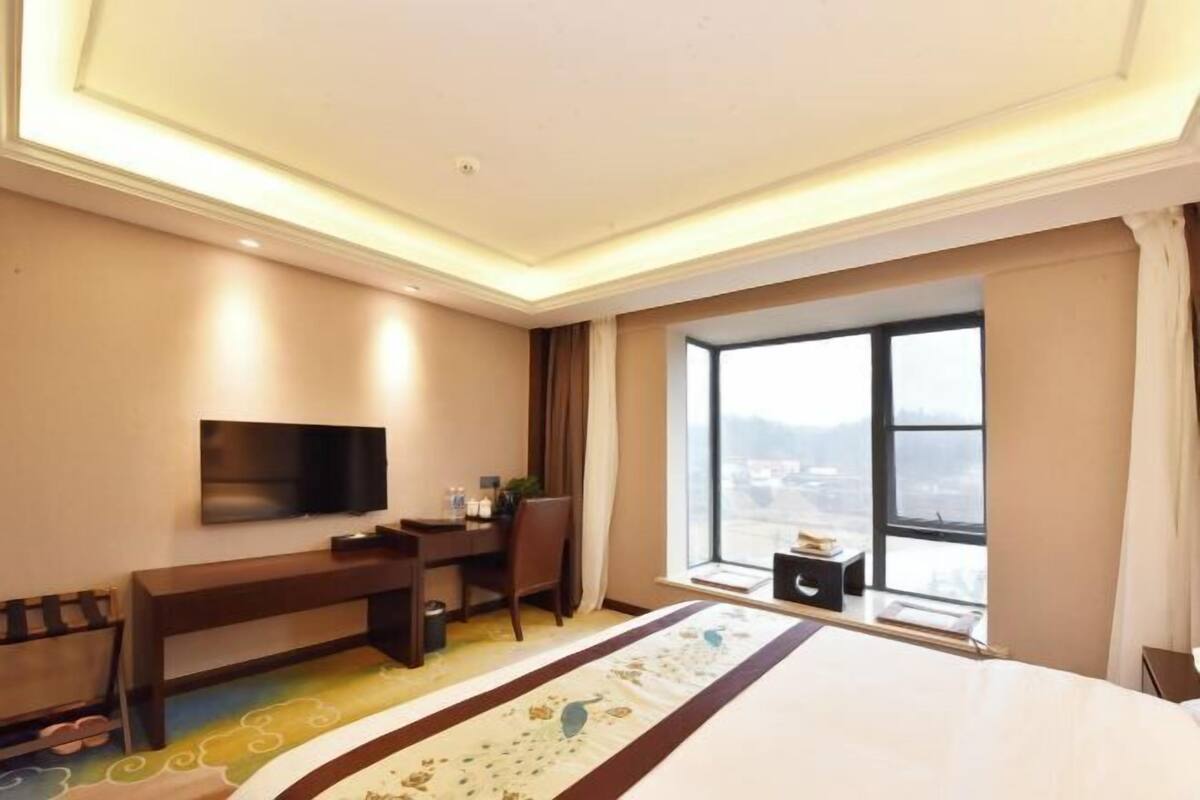 A hotel room with a bed, a desk, a chair, a TV, and a large window with a view.