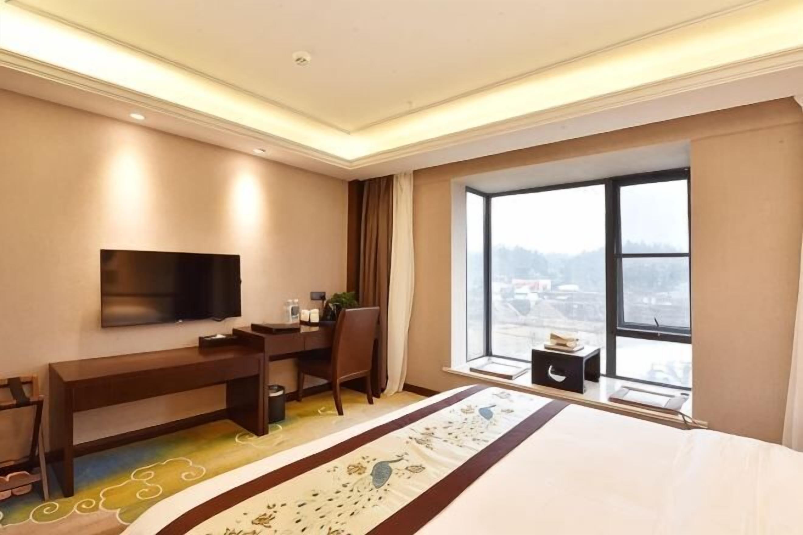 Habitación de hotel con cama, escritorio, silla, televisión y una ventana grande con vistas.