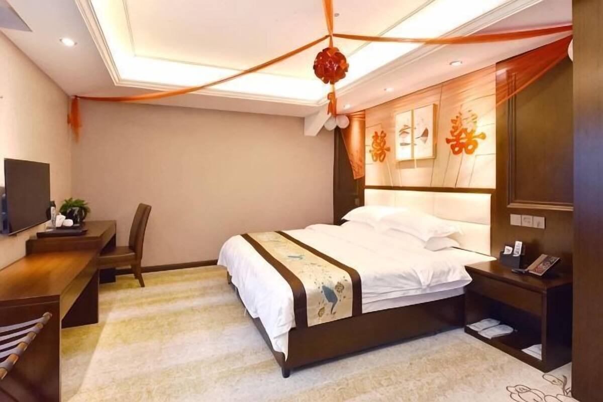 A hotel room with a bed, bedside table, TV, desk, and chair.