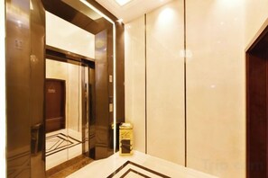 An elevator with a mirrored wall, a small trash bin, and a marble floor. - Fenghuag Xidi Hotel (Jinzhai)