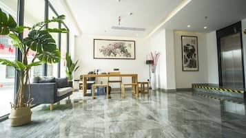 A modern hotel lobby with a marble floor, a sofa, a dining table, and large windows.