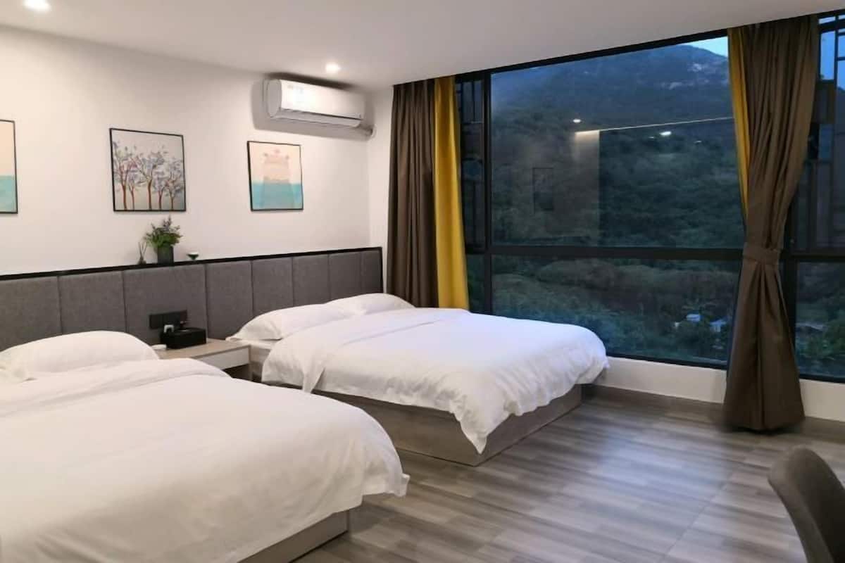 A hotel room with two beds, a large window with curtains, a wall-mounted air conditioner, and framed artwork.