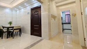 Een hotellobby met een eetgedeelte, een donkere houten deur en een gang die naar een badkamer leidt.