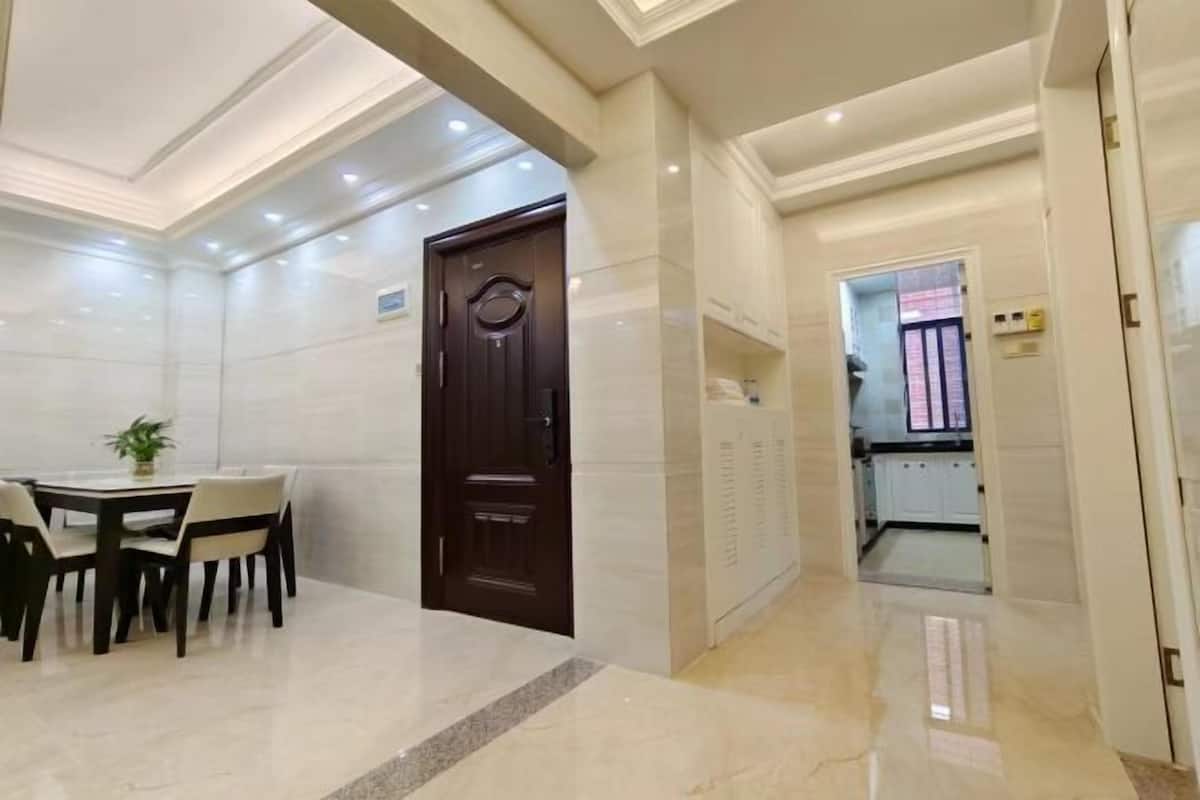 A hotel lobby with a dining area, a dark wooden door, and a corridor leading to a bathroom.