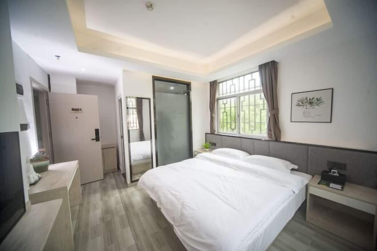 A modern hotel room with a large bed, a desk, a wardrobe, and a window with curtains.