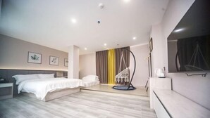Een moderne hotelkamer met een bed, nachtkastjes, een zithoek met een hangstoel en een groot raam met gordijnen.