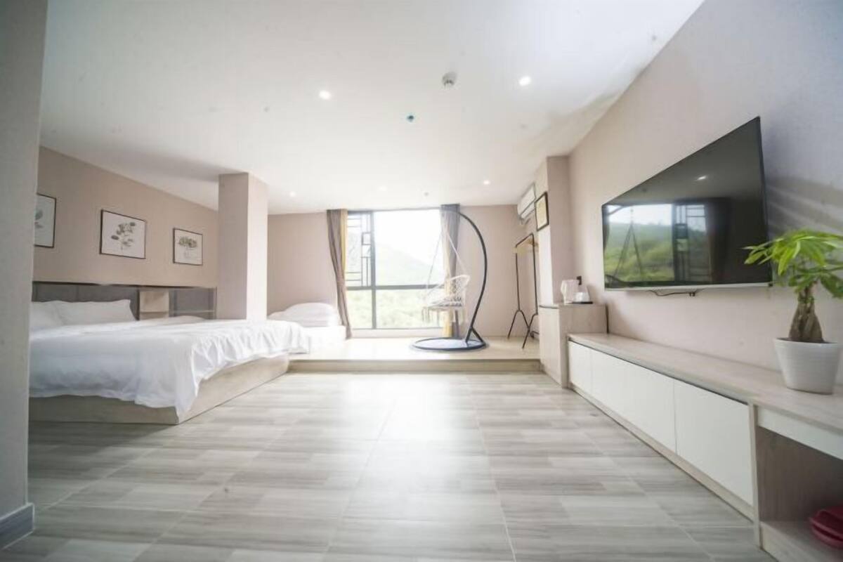 A modern bedroom with a bed, a TV mounted on the wall, and a large window.
