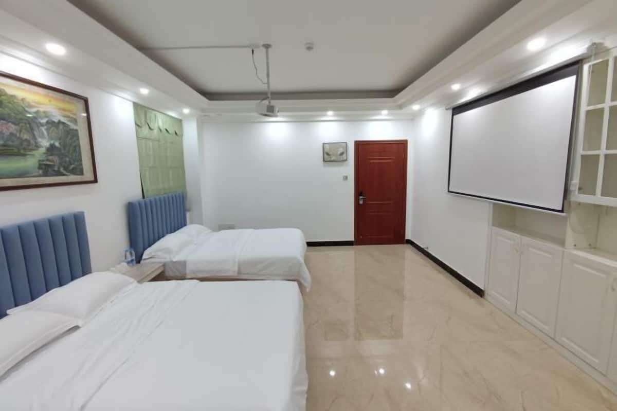 A hotel room with two beds, a projector screen, a painting, and a red door.