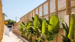 A narrow pathway lined with large banana plants and a woven wall. - ATMA BEACH ROOMS & SUITES (Rhodes)
