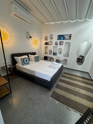 A modern bedroom with a bed, bedside tables, a wall-mounted shelf with books, and a unique ceiling design. - Olvion Luxury Living (Kassandra)