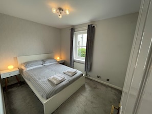 Um quarto com cama, abajures, janela com cortinas e luminária no teto.