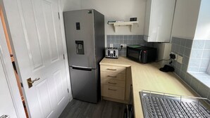 Eine kleine Küche mit Kühlschrank, Toaster, Mikrowelle und einem Schrank über der Arbeitsfläche.