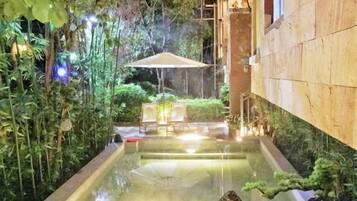 Área de piscina interior tranquila, com superfície de água límpida, rodeada por vegetação exuberante e um espaço de estar com mesa e cadeiras.