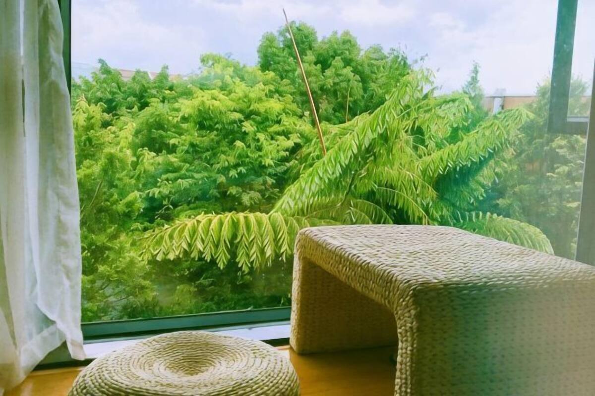 Una habitación con un ventanal grande, un banco tejido y un taburete tejido.