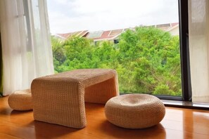 A room with a large window, a wooden floor, and a woven pouf.