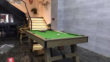 A pool table in a room with a staircase and a bar area.