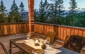 An outdoor dining area with a table set for two, surrounded by a wooden railing with a scenic mountain view in the background.