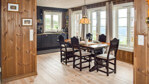Un coin repas avec une table et des chaises en bois, un luminaire suspendu et de grandes fenêtres avec des rideaux.