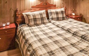 A bed with a plaid bedspread, two pillows, and a wooden headboard. There are two nightstands with decorative items on them.