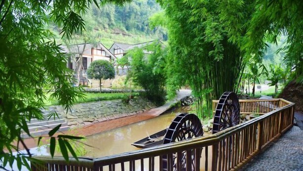 A traditional water wheel structure in a lush, green setting with stone pathways and bamboo trees. - Mufu Leisure Mountian Resort (Muchuan)