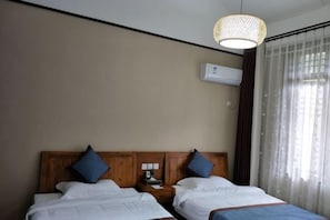 A hotel room with two beds, a wooden headboard, a bedside table with a lamp, and an air conditioning unit on the wall. - Mufu Leisure Mountian Resort (Muchuan)