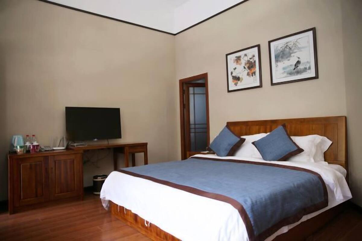 A hotel room with a wooden bed, a television, a desk, and two framed artworks on the wall.