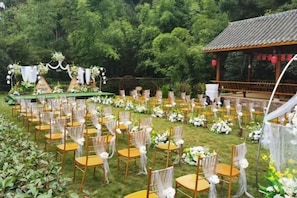 An outdoor wedding venue with rows of chairs and tables, a stage with floral decorations, and a gazebo in the background. - Mufu Leisure Mountian Resort (Muchuan)