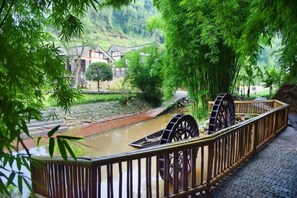 A riverside walkway with a traditional water wheel, bamboo trees, and a stone bridge. - Mufu Leisure Mountian Resort (Muchuan)